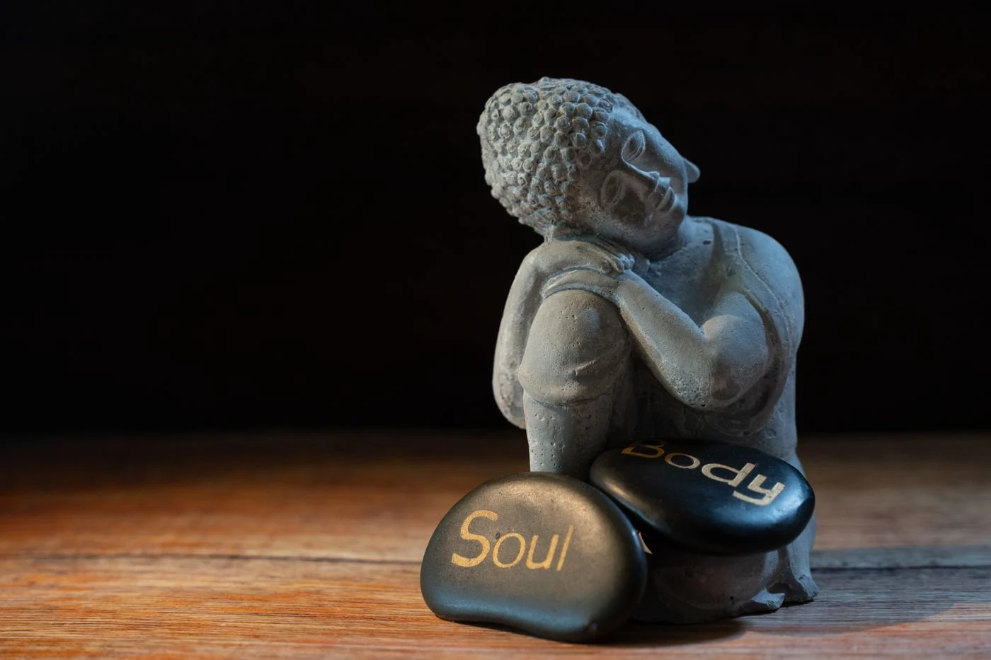 Figura de Buda en reposo junto a piedras sobre una superficie de madera iluminada suavemente